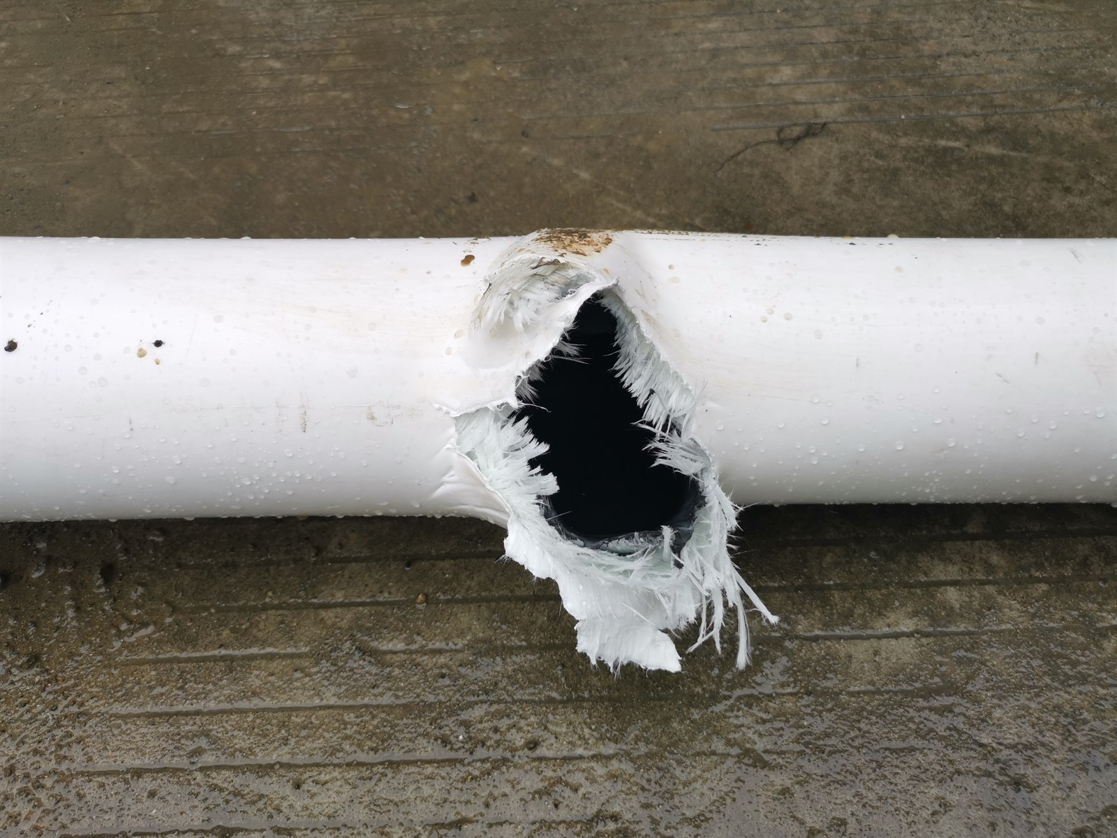 Close-up of a burst failure in the outer jacket and reinforcement layers of a reinforced thermoplastic pipe