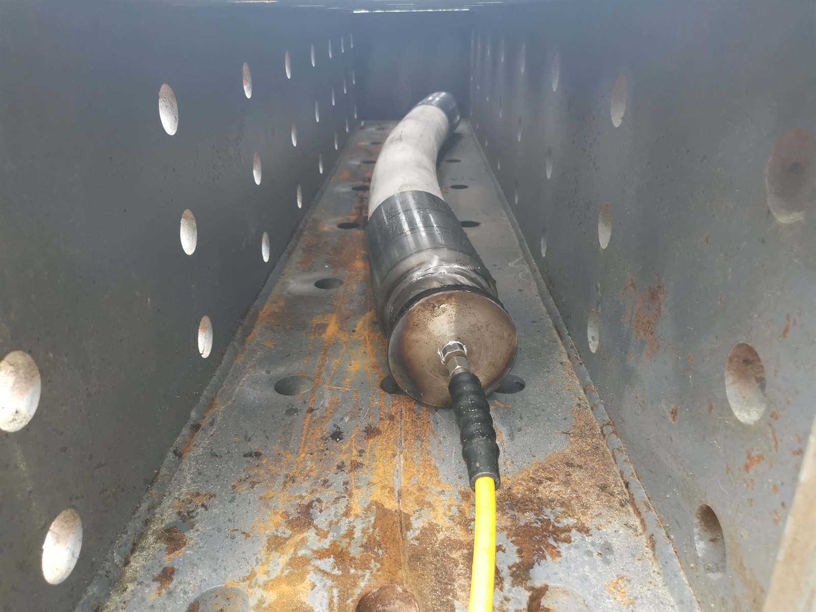 Reinforced thermoplastic pipe specimen secured inside a steel burst-test enclosure with a high-pressure hose connected
